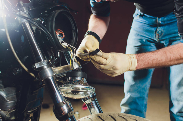 Man fixing bike. Confident young man repairing motorcycle near his garage. replacement lamp in the headlamp - Φωτογραφία, εικόνα