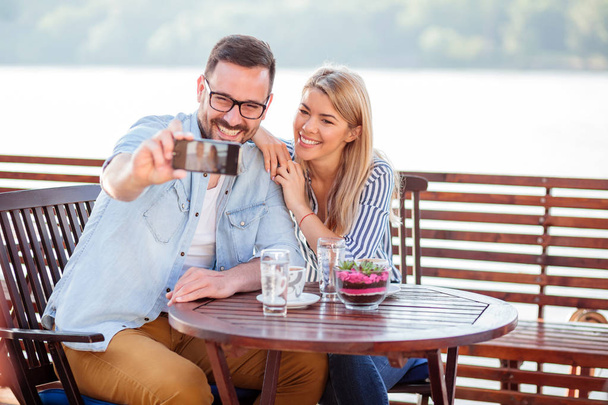 カフェでコーヒーを飲んで幸せな若いカップルは、自分撮りを取って - 写真・画像