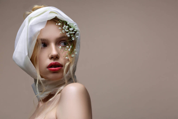 Model with white silk scarf on her head posing near background - Foto, afbeelding