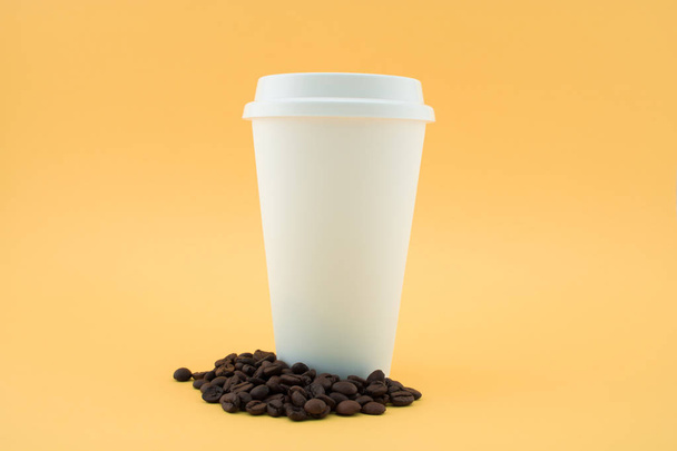 Kaffeetasse aus Papier auf Kaffeebohnen, gelber Hintergrund. Kaffeetasse abgedeckt. - Foto, Bild