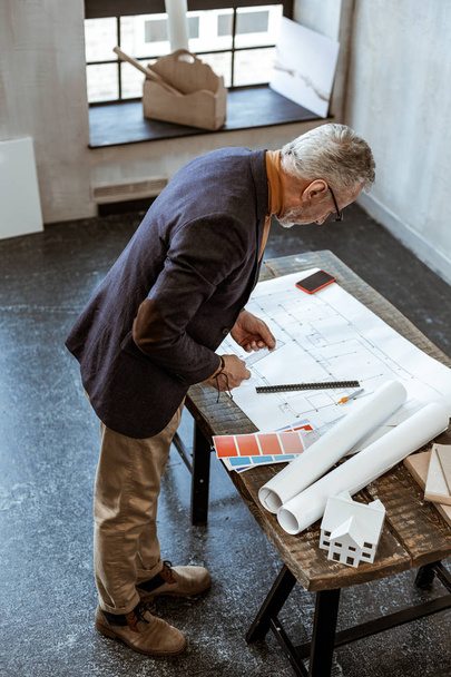 Grey-haired interior designer looking at the map of apartment - Foto, afbeelding