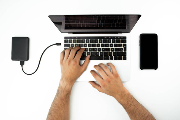 Τα χέρια ενός επιχειρηματία που χρησιμοποιεί τον φορητό υπολογιστή του και το smartphone του. - Φωτογραφία, εικόνα