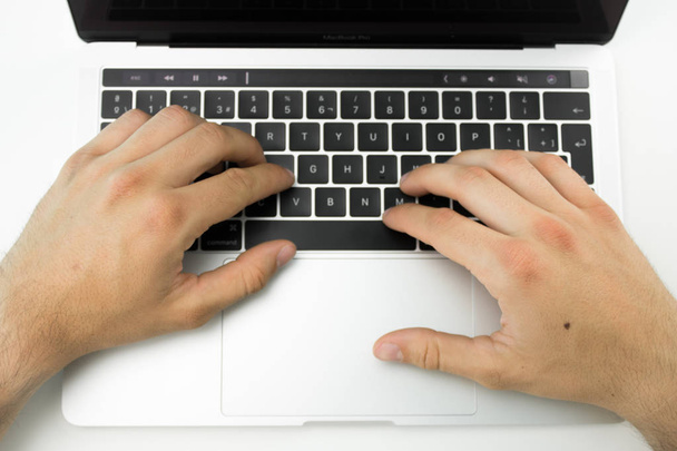 Hands using the keyboard and touchpad of a laptop computer on a white table. - 写真・画像