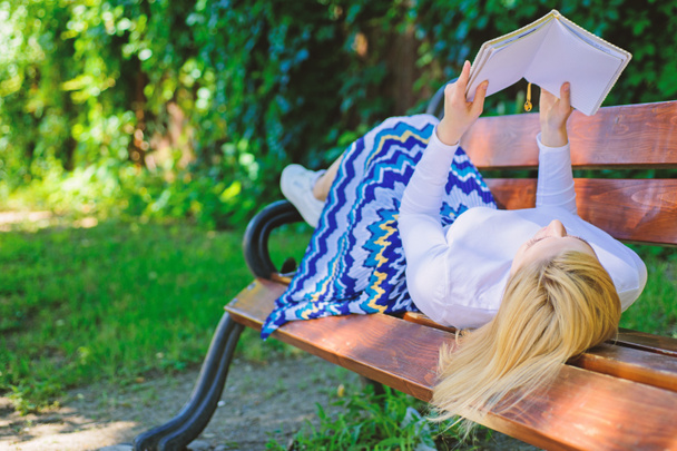 Девушка лежала скамейка парк отдыха с книгой, зеленый фон природы. Женщина проводит досуг с книгой. Интересная книга. Умная и красивая. Девушка читает на открытом воздухе, расслабляясь на скамейке. Умная леди расслабляется
 - Фото, изображение