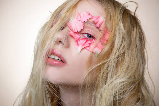 Model with messy blonde hair posing with flower near eye - Foto, afbeelding
