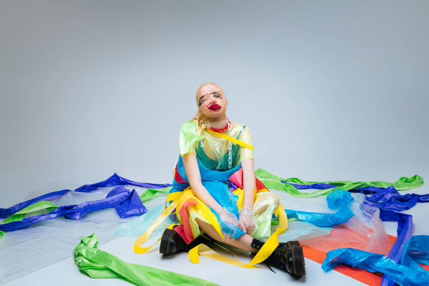 Model sitting on the floor surrounded by colorful plastic - 写真・画像