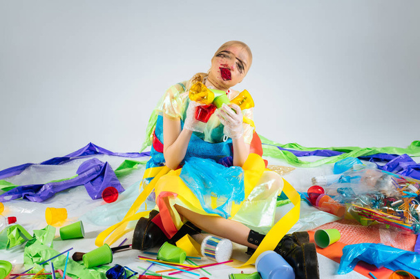 Model wearing plastic clothes sitting on floor surrounded by plastic trash - Valokuva, kuva