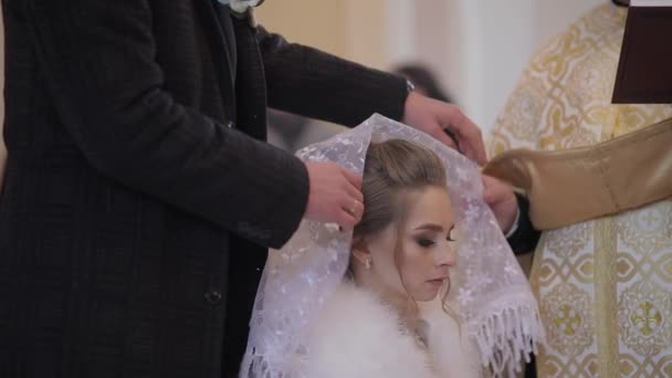 Elegáns menyasszony egy régi templomban. Egy férfi sálat visel a fejét a felesége - Felvétel, videó
