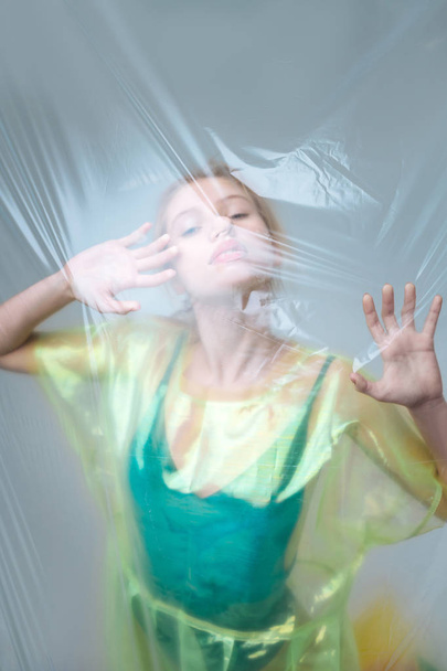 Model wearing green clothing posing behind transparent plastic sheet - 写真・画像