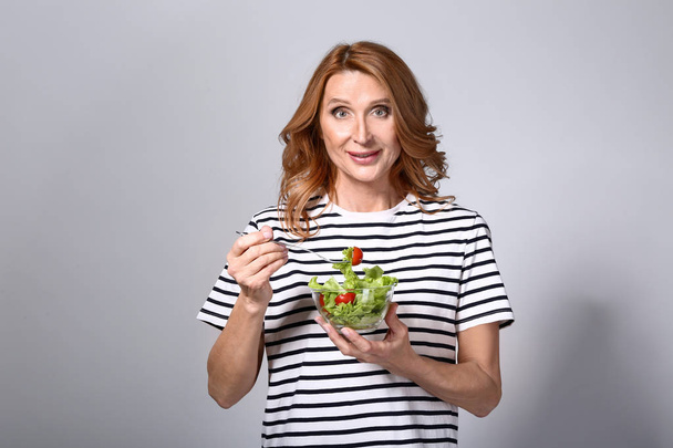 Donna matura con ciotola di insalata di verdure su sfondo grigio
 - Foto, immagini