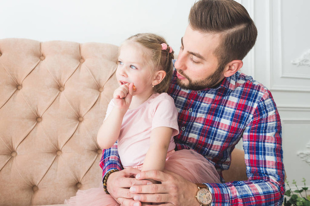 Cute little girl with a lollipop sitting with dad on the couch. - Foto, Bild