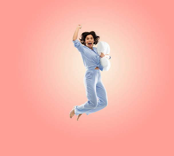 happy woman in blue pajama jumping with pillow - Φωτογραφία, εικόνα