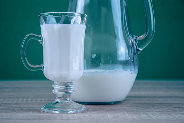 Склянка молока стоїть на столі. Молоко вливають у кухоль. Здорова їжа. Зелений фон
. - Фото, зображення