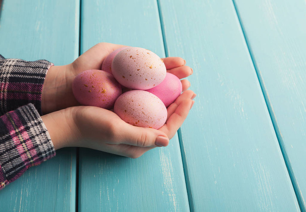 Woman holding pink colored easter eggs on blue table - 写真・画像