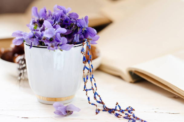 Bodegón con violeta en copa blanca, libros viejos. Romántico fondo floral de primavera
. - Foto, Imagen