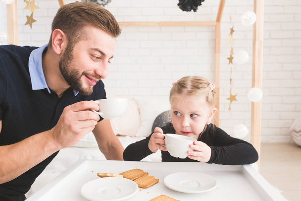 Cute little girl and her father drink tea with cookies at home. - Fotoğraf, Görsel