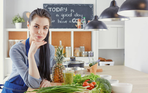 Ευτυχισμένος νεαρή γυναίκα στην κουζίνα με φρέσκα λαχανικά στο τραπέζι - Φωτογραφία, εικόνα