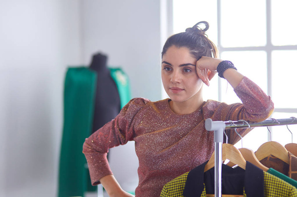 Bela jovem estilista segurando prancheta perto de rack com design
 - Foto, Imagem