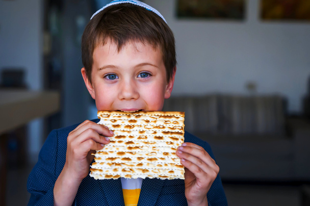 Carino ragazzo ebreo caucasico che tiene in mano e prende un morso da un tradizionale pane azzimo ebreo azzimo. Ebraico Pesach immagine concetto Pesach
. - Foto, immagini