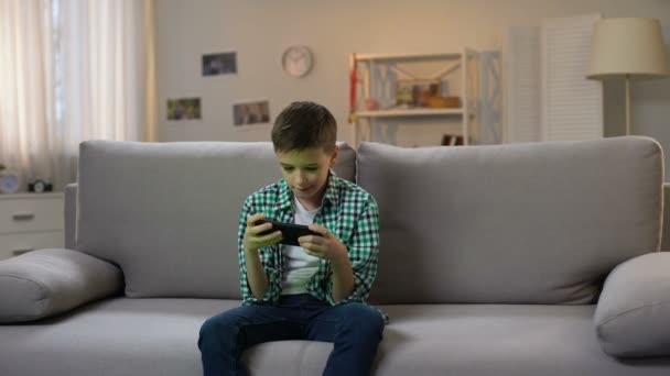 Preschool boy procrastinating and playing game on smartphone, gadget addiction - Video, Çekim