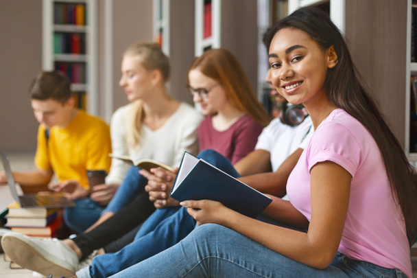 Group of diverse classmates sitting on floor at library - Photo, image