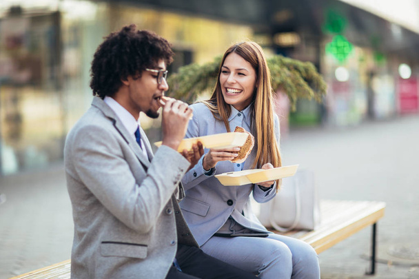 Χαμογελαστοί επιχειρηματίες με σάντουιτς που κάθονται μπροστά από τον υπάλληλο - Φωτογραφία, εικόνα