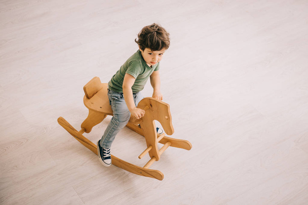 overhead view of little boy in green t-shirt riding on rocking horse - Zdjęcie, obraz