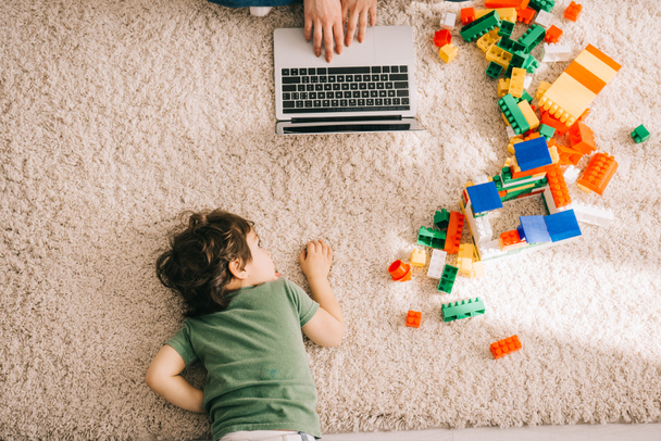 Przycięte widok matki za pomocą laptopa i syna leżącego na dywanie - Zdjęcie, obraz