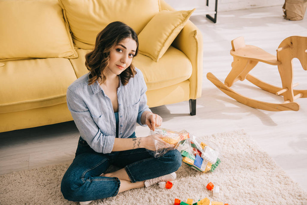 Frau mit Spielzeugklötzen sitzt mit überkreuzten Beinen auf Teppich  - Foto, Bild