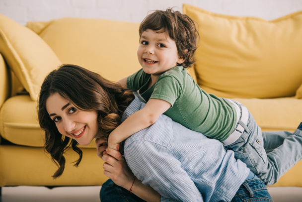 Χαμογελαστή μητέρα και γιος παίζοντας μαζί κοντά σε κίτρινο καναπέ - Φωτογραφία, εικόνα
