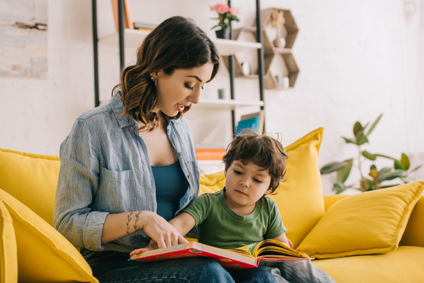 Mom and son sitting on yellow sofa and reading book - Photo, image
