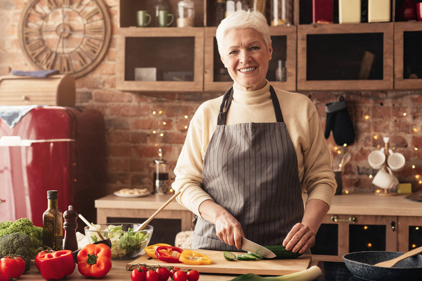 Весела старша жінка, що ріже овочі для салату
 - Фото, зображення