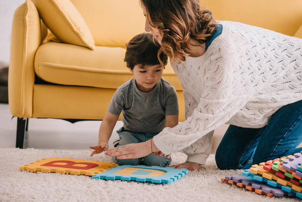 Mother and son playing with alphabet puzzle mat on carpet - 写真・画像