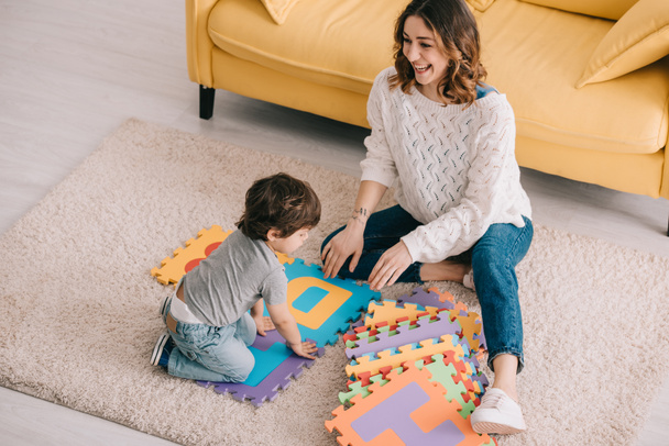 Mother and son playing with alphabet puzzle mat on carpet - Foto, imagen