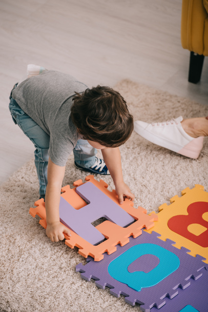 child playing with alphabet puzzle mat on carpet - Foto, Imagen