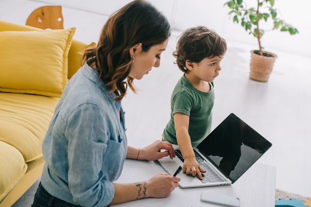 kid touching laptop while mother working in living room - Photo, Image