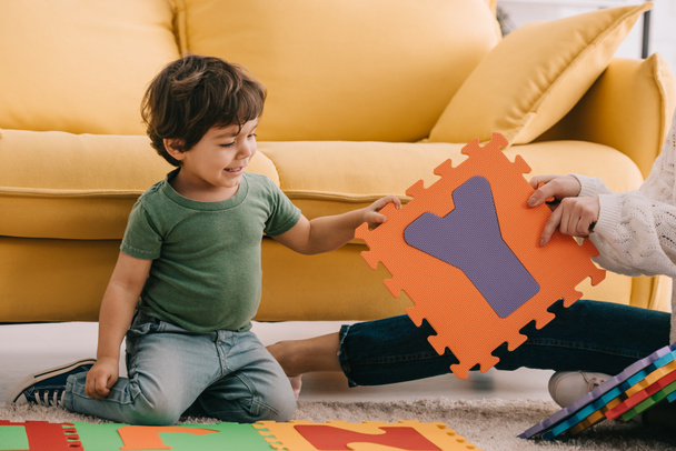Ausgeschnittene Ansicht von Mutter und Sohn beim Spielen mit Buchstabenpuzzle-Matte auf Teppich - Foto, Bild