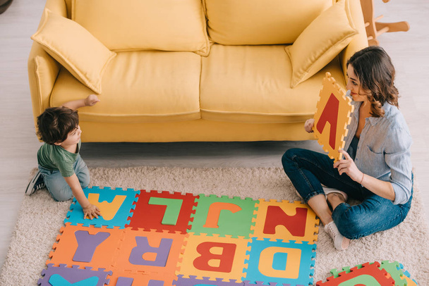 overhead view of smiling mother and kid playing with alphabet puzzle mat - Fotografie, Obrázek