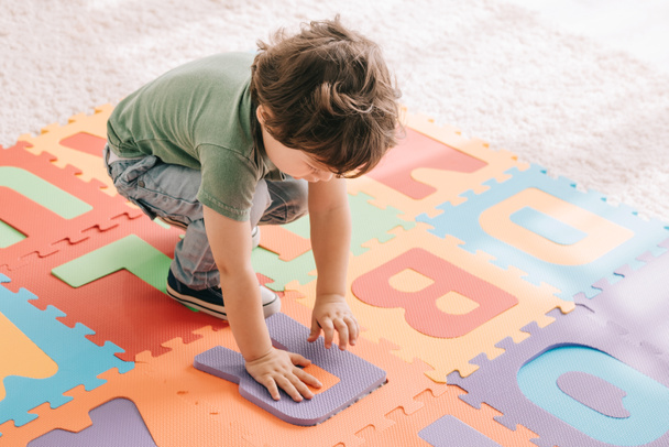 Aranyos gyerek, zöld póló játszik a puzzle mat - Fotó, kép