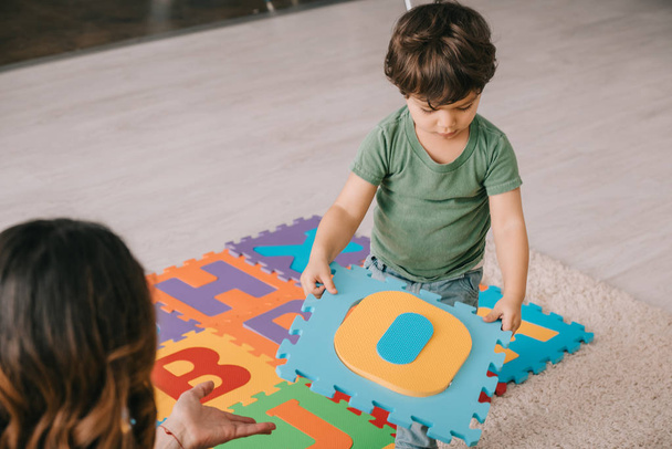 vista ritagliata di madre e figlio apprendimento alfabeto con tappetino puzzle
 - Foto, immagini