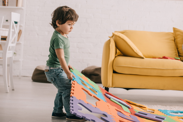 Vista completa de niño en camiseta verde jugando con alfombra de rompecabezas
 - Foto, Imagen