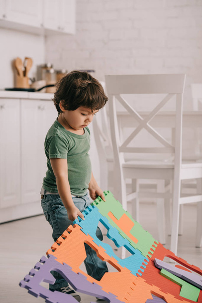 Niedliches Kind im grünen T-Shirt spielt mit Puzzle-Matte - Foto, Bild