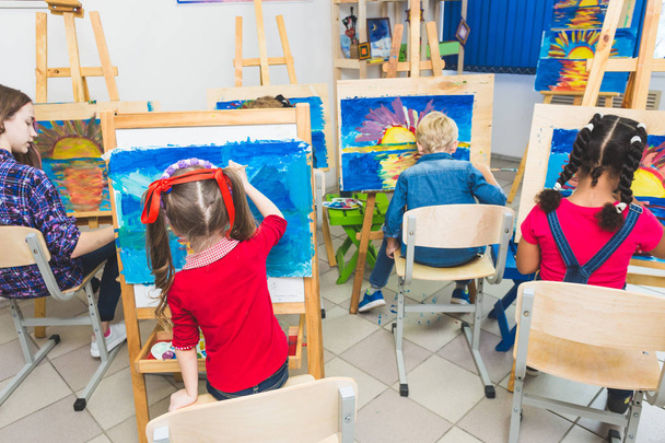 A group of preschool students and young teacher in drawing class paint in gouache. mixed race schoolgirl afroamerican and boy. Artwork - Фото, зображення