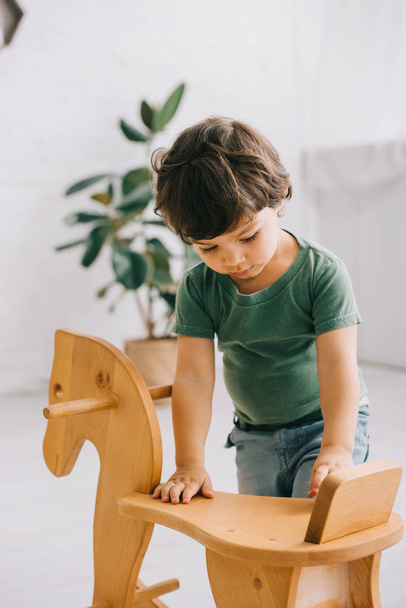 Toddler boy in green t-shirt and wooden rocking horse - Zdjęcie, obraz