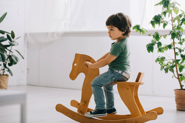 child sitting on wooden rocking horse in living room - Foto, Imagen