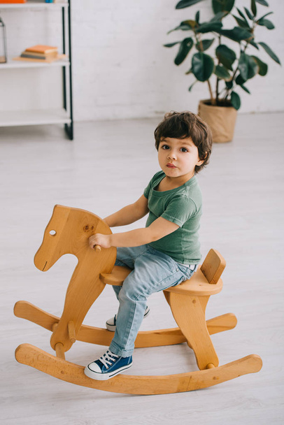 kid sitting on wooden rocking horse in living room - Zdjęcie, obraz