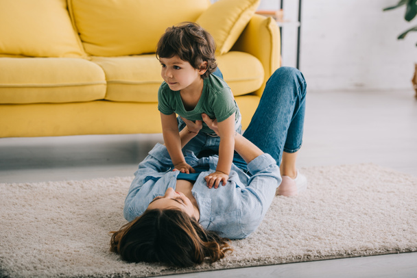 Happy mother and son playing on carpet in living room - Foto, Imagem