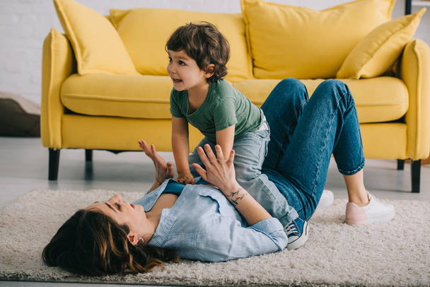 Happy mother and son playing on carpet in living room - Photo, Image