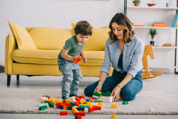 Mother and son playing with lego on carpet in living room - Foto, Imagen