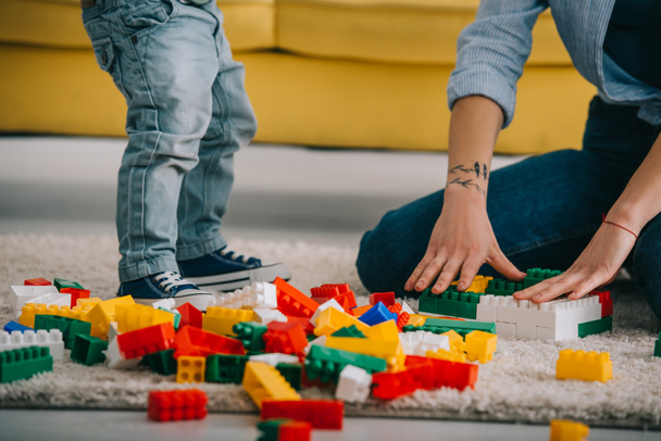 cropped view of mother and son playing with lego on carpet in living room - 写真・画像